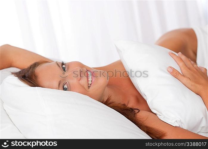 Smiling woman lying in white bed, looking at camera