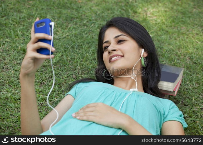 Smiling woman lying on grass listening to mp3 player