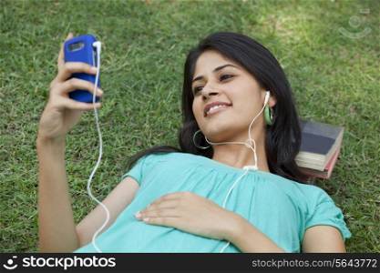 Smiling woman lying on grass listening to mp3 player