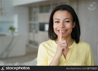 Smiling woman makes silence gesture at home sharing secret about online store offer, discounts, sale. Happy friendly female asking to shush, keep private information, looking at camera.. Smiling woman makes silence gesture at home sharing secret about online store offer, discounts, sale