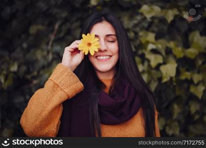 Smiling woman playing with a yellow flower in field