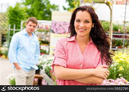 Smiling woman posing at garden centre young man in background