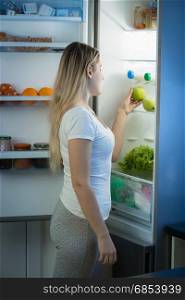 Smiling woman posing at open fridge at late evening