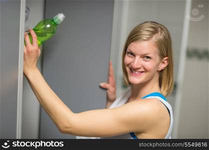 Smiling woman putting water bottle in locker at healthclub