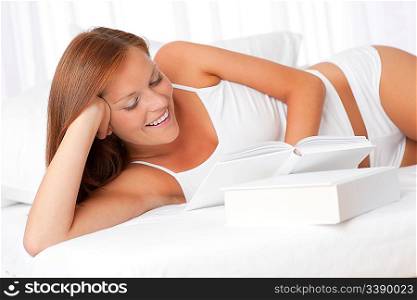Smiling woman reading book lying on white sofa