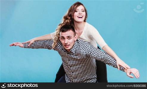 Smiling woman riding piggyback on man shoulders. Happy young couple having fun together in studio on blue.. Woman riding piggyback on man. Happy couple.