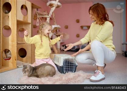 Smiling woman showing cat in cage to little bit scared cute girl child. Fun time in pet shelter. Smiling woman showing cat in cage to little bit scared cute girl child