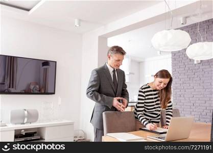 Smiling woman signing contract while standing by mature male realtor at table in apartment
