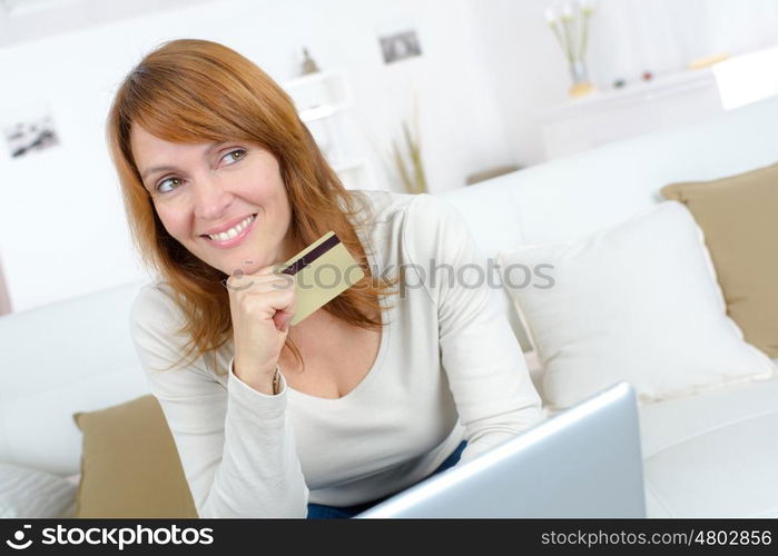 smiling woman sitting on a sofa and holding credit card