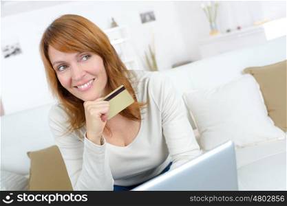 smiling woman sitting on a sofa and holding credit card