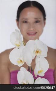 Smiling woman standing behind a bunch of beautiful white flowers, studio shot