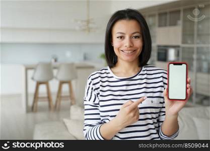 Smiling woman tenant showing at smartphone with blank screen at home. Female pointing with finger at mockup phone screen, recommending services for housing search. Mobile apps advertising.. Tenant woman pointing at phone with mock up blank screen reccomends app of renting service at home