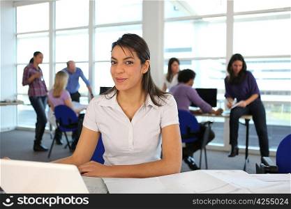 Smiling woman using a laptop in a busy office