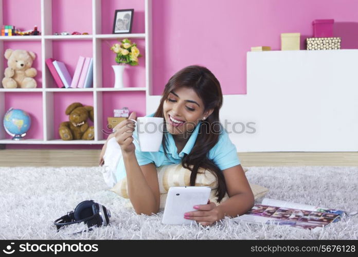 Smiling woman using digital tablet while drinking coffee at home