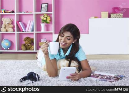 Smiling woman using digital tablet while drinking coffee at home