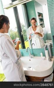 Smiling woman using skin care lotion bathroom morning bathrobe preparation