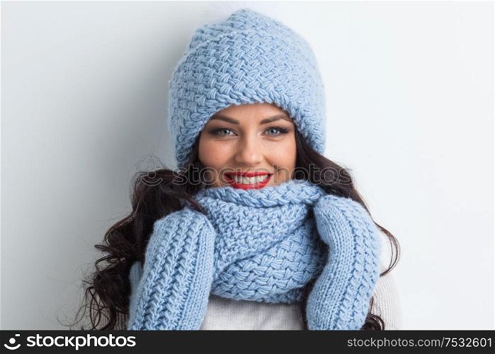 Smiling woman wearing blue knitted winter hat, scarf and mittens. Woman in blue winter hat