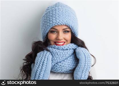 Smiling woman wearing blue knitted winter hat, scarf and mittens. Woman in blue winter hat