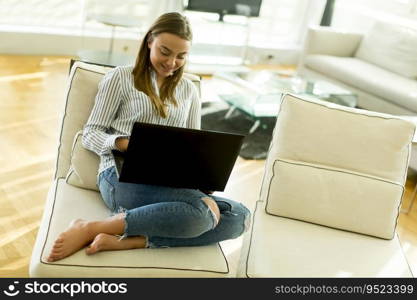 Smiling woman with a laptop lying on a sofa in her living room