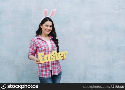 smiling woman with bunny ear showing easter word against blue textured background