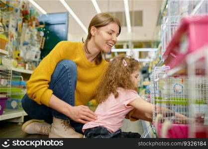Smiling woman with her daughter choosing hamster or other rodent at pet shop. Happy family enjoying purchase new pet. Smiling woman with her daughter choosing hamster or other rodent at pet shop