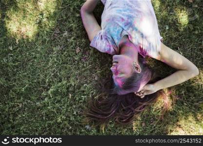 smiling woman with holi colors lying green grass