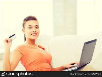 smiling woman with laptop showing credit card at home