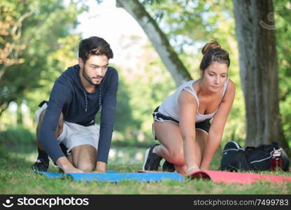 smiling woman with personal trainer doing exercises on mat outdoors