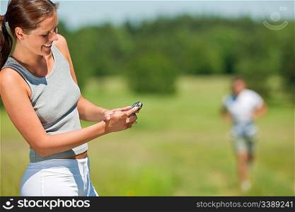 Smiling woman with stopwatch measuring time, man in background, shallow DOF