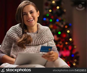 Smiling woman with tablet PC and credit card in front of Christmas tree
