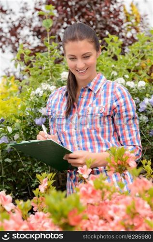 Smiling woman worker doing inventory of flowers at garden center