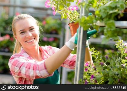 Smiling woman working in garden center with potted flowers sunny