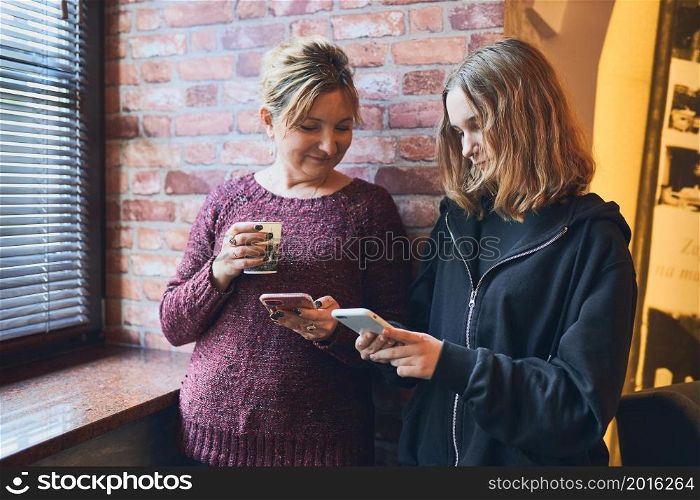 Smiling women using smartphones drinking coffee charging mobile phone relaxing in office while taking a break