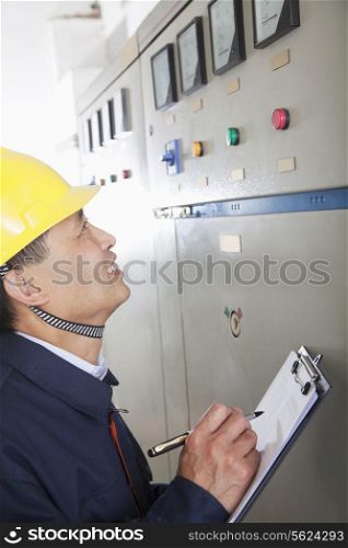 Smiling worker holding clipboard and checking controls in a gas plant, Beijing, China