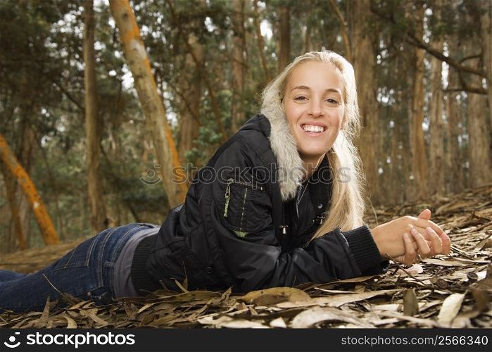 Smiling young adult Caucasian woman lying on ground in forest.