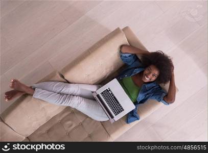 Smiling young African American woman using laptop while relaxing on sofa at luxury home top view