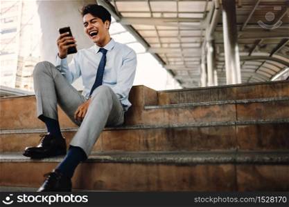 Smiling Young Asain Businessman Using Mobile Phone in the City. Sitting at the Staircase