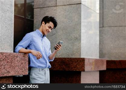 Smiling Young Asian Businessman Using Mobile Phone in the City