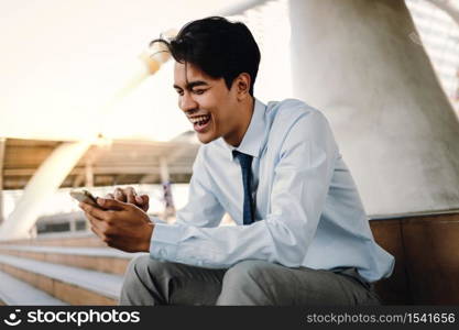 Smiling Young Asian Businessman Using Mobile Phone in the City. Sitting at the Staircase