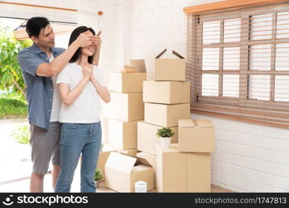 Smiling young Asian happy couple close girlfriend eyes for a surprise at moving day in their new home after buying real estate. Concept of starting a new life for a newly married couple.