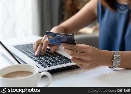 Smiling young Asian woman holding credit card while using computer laptop at home office, digital lifestyle with technology, e-commerce, shopping online concept.