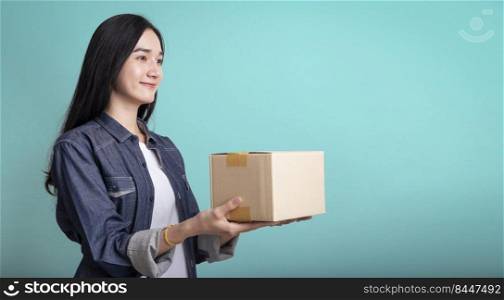 Smiling young beautiful asian woman carrying a parcel post box isolated on blue background , delivery woman and jacket holding boxes in hands