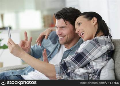 smiling young beautiful couple holding smartphone and taking selfie