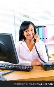 Smiling young black business woman on phone at desk in office