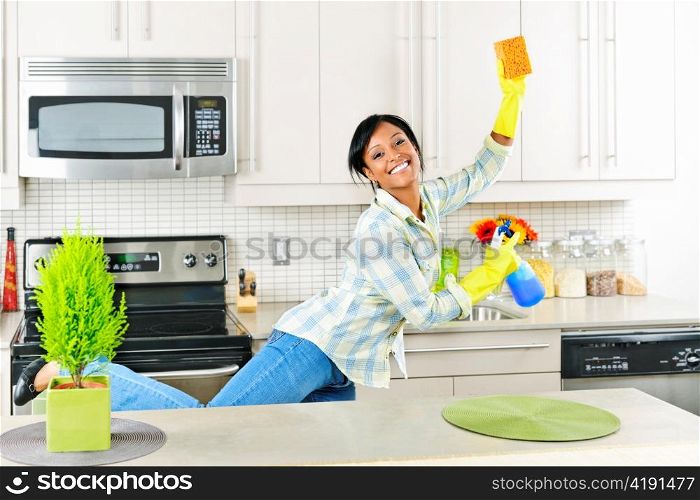 Smiling young black woman dancing and enjoying cleaning kitchen