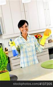Smiling young black woman with sponge and rubber gloves cleaning kitchen