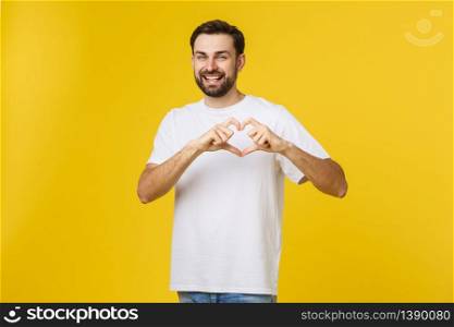 smiling young boy making heart gesture on his chest with white shirt isolated on yellow background.. smiling young boy making heart gesture on his chest with white shirt isolated on yellow background