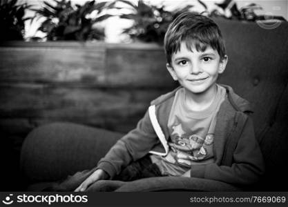 smiling young boy sitting on the sofa looking at camera, black and white shot. smiling young boy sitting on the sofa