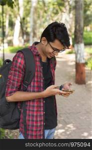Smiling young boy with backpack looking at his smart phone and texting