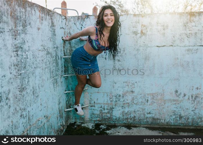 Smiling young brunette woman with bikini in an old empty pool playing with ladder